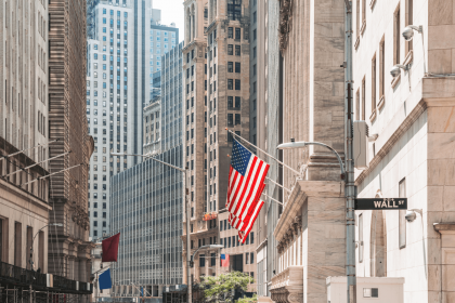 Wall Street with American flag, representing financial markets and economic activity.