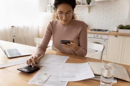 A woman using a smartphone and calculator to manage her bills.