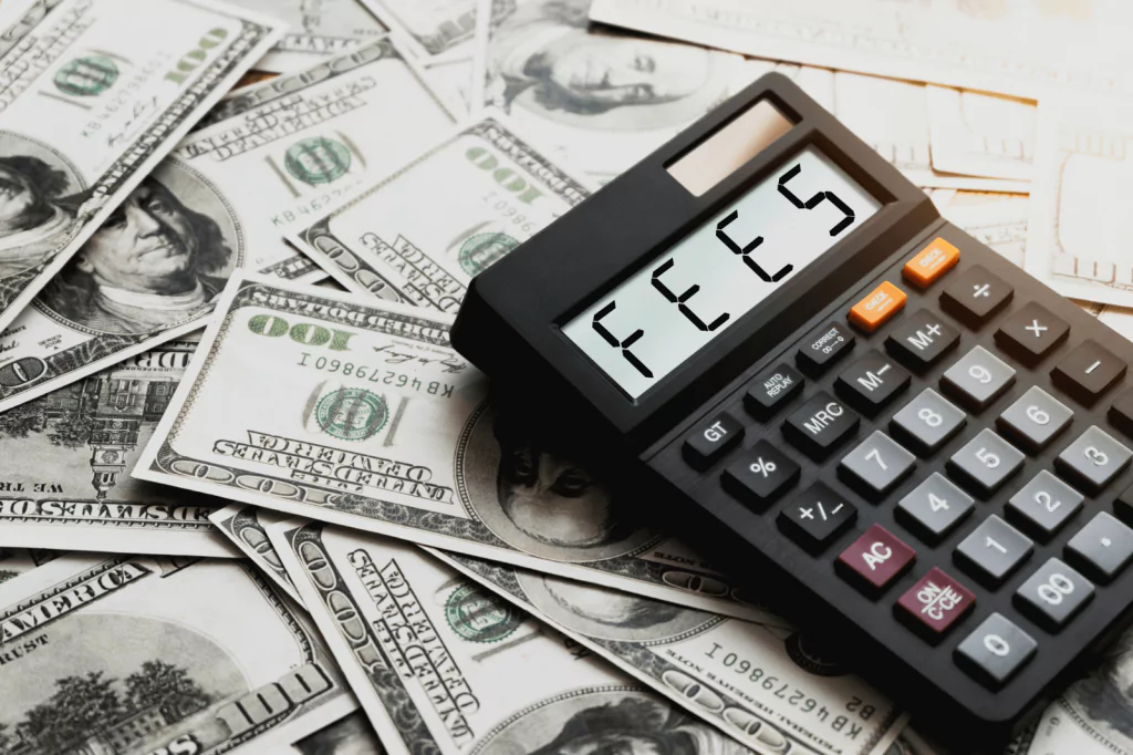 Calculator displaying the word "Fees" on a background of dollar bills