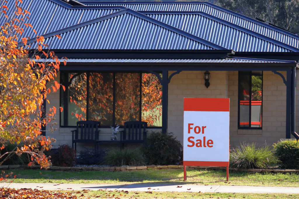 A house for sale sign in front of a suburban home.