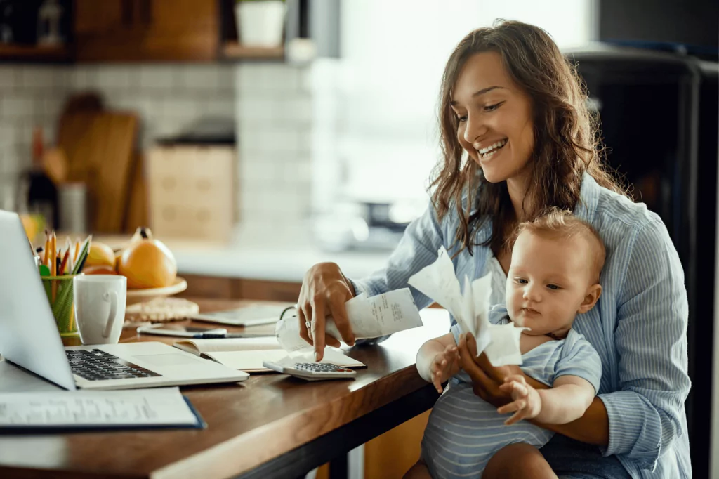 Mother budgeting at home while holding her baby.
