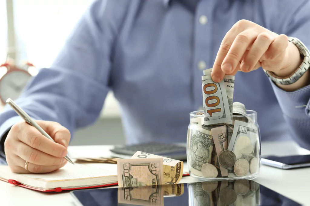 Person saving money in a jar while taking notes.