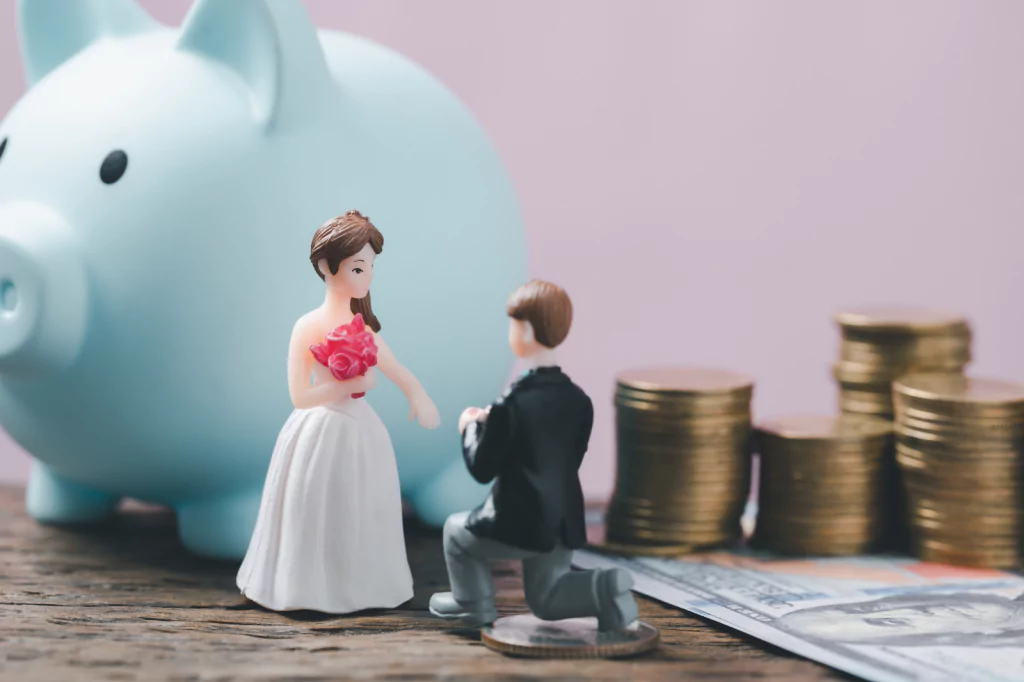 Bride and groom figurines in front of a piggy bank and stacks of coins