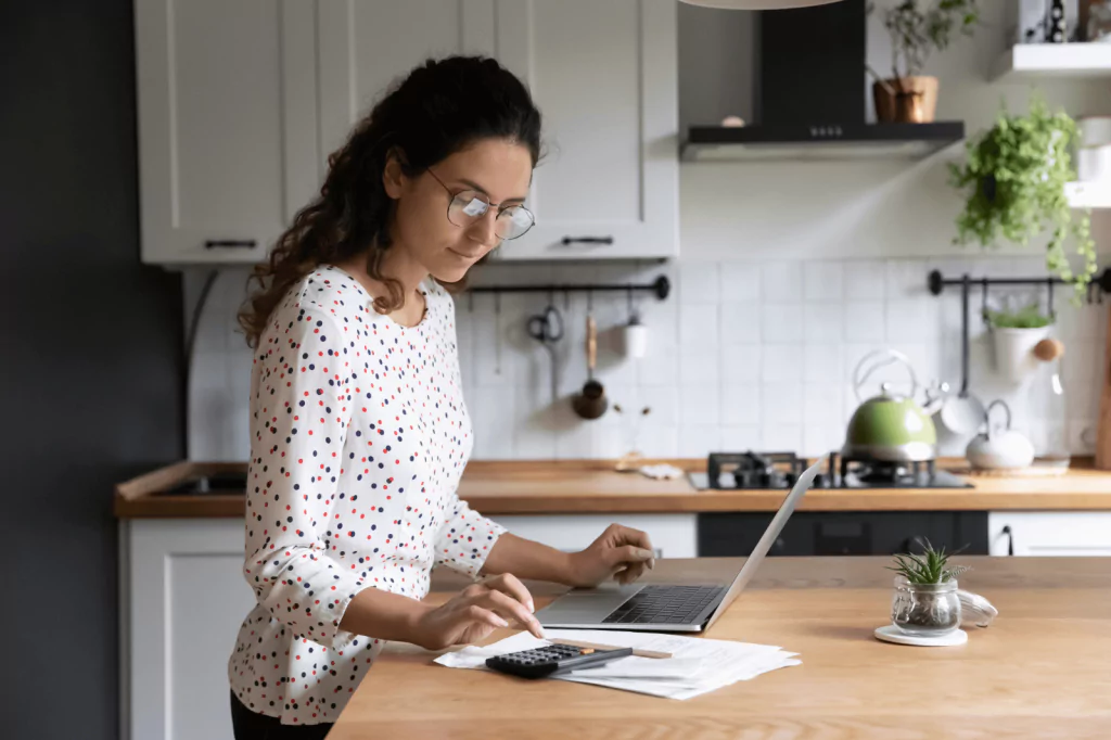 Woman calculating her expenses with a laptop and calculator.