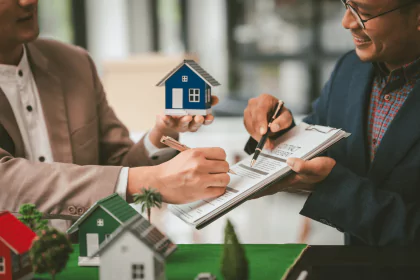 Two people signing mortgage application documents while holding a model house